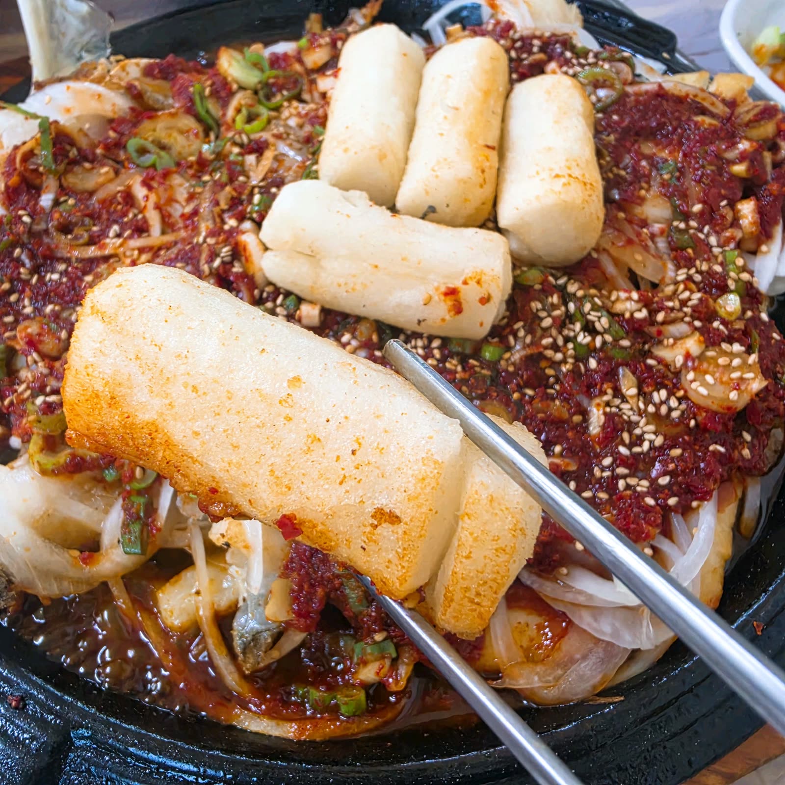 재진이네아구찜 동래본점 대구뽈구이에서 젓가락으로 들어 올린 가래떡과 양념 묻은 대구살
