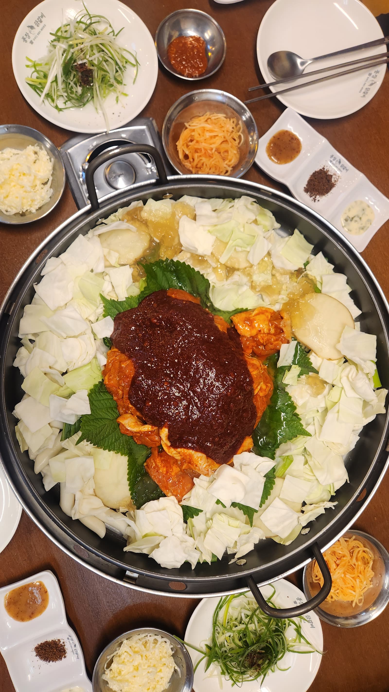 풍장닭갈비 본점 생닭갈비 상차림, 양배추 위에 양념 닭갈비와 깻잎이 올라간 철판과 밑반찬