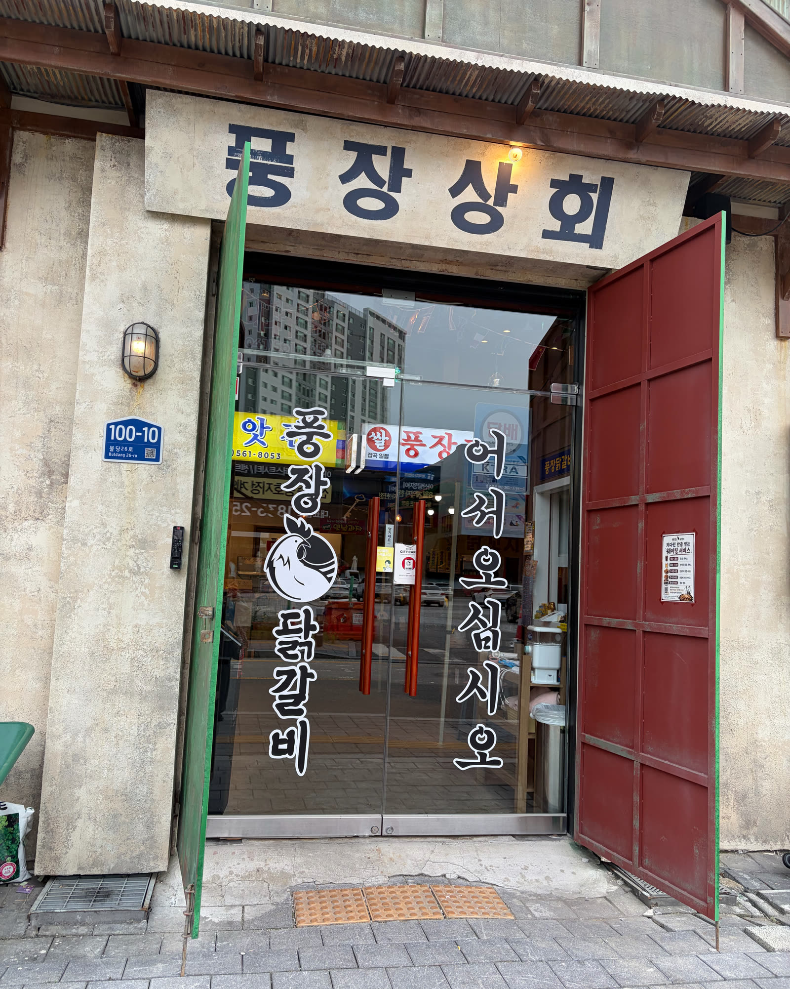 풍장상회라고 쓰인 풍장닭갈비 본점 입구, 초록 철문과 빨간 철문 사이 유리문에 닭 로고가 붙어 있다