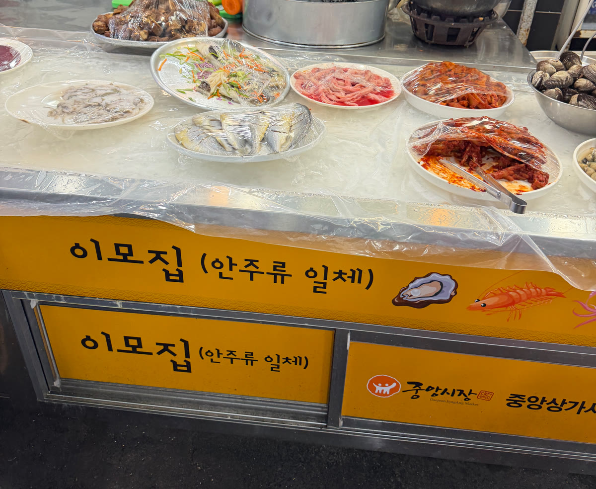 이모집 노란 간판과 좌판, 대전중앙시장 상가 매대에 안주 접시가 올려진 모습