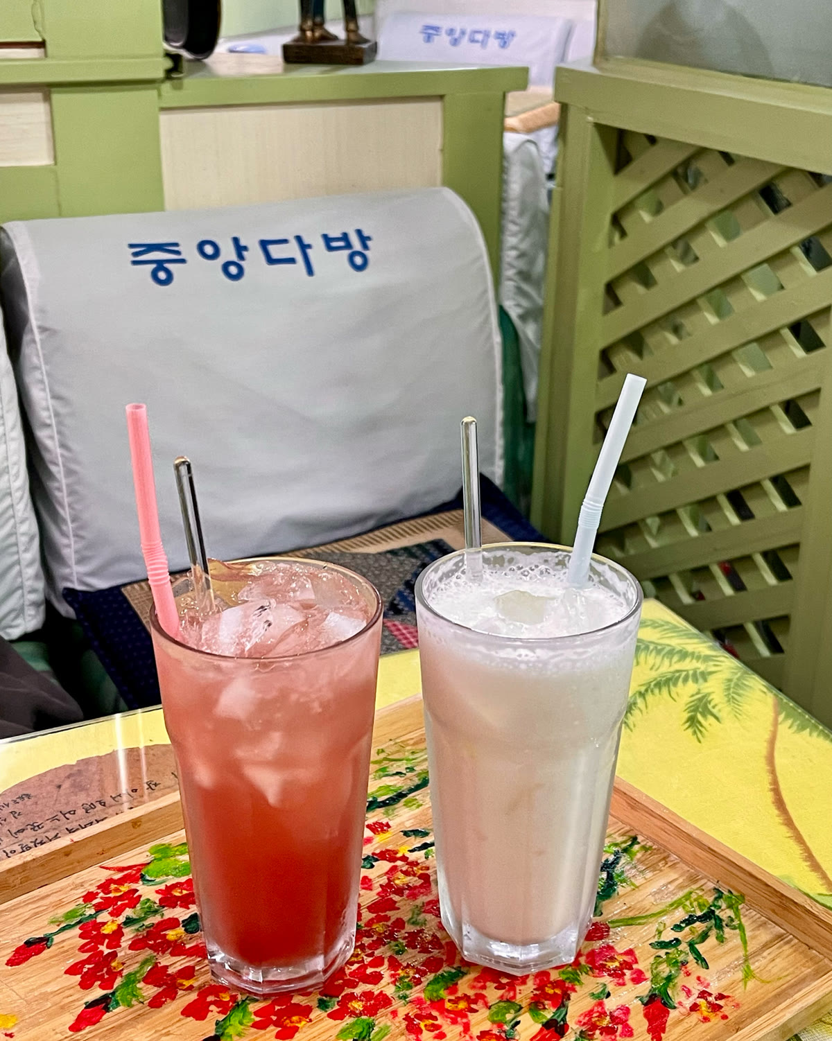 중앙다방 의자커버 앞에 놓인 음료 두 잔, 꽃무늬 쟁반 위 주스와 미숫가루