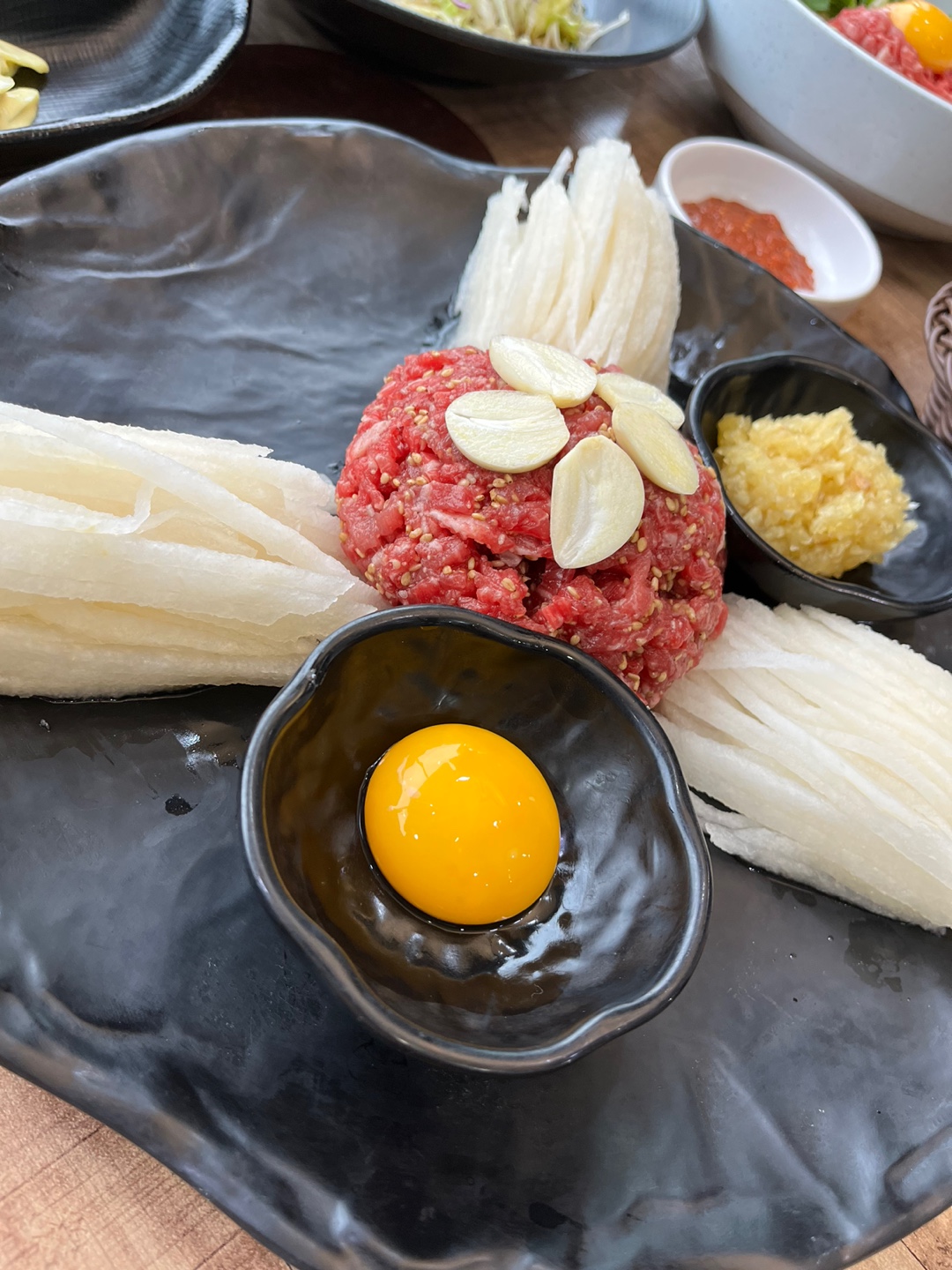 단양 다원 한우 마늘육회, 검은 그릇에 육회와 달걀노른자, 배채, 마늘이 함께 담긴 모습