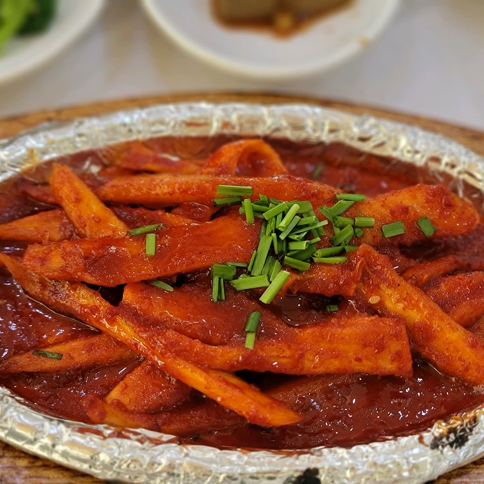 은박 접시에 담긴 매콤한 양념 생선, 쪽파 고명이 올라간 클로즈업