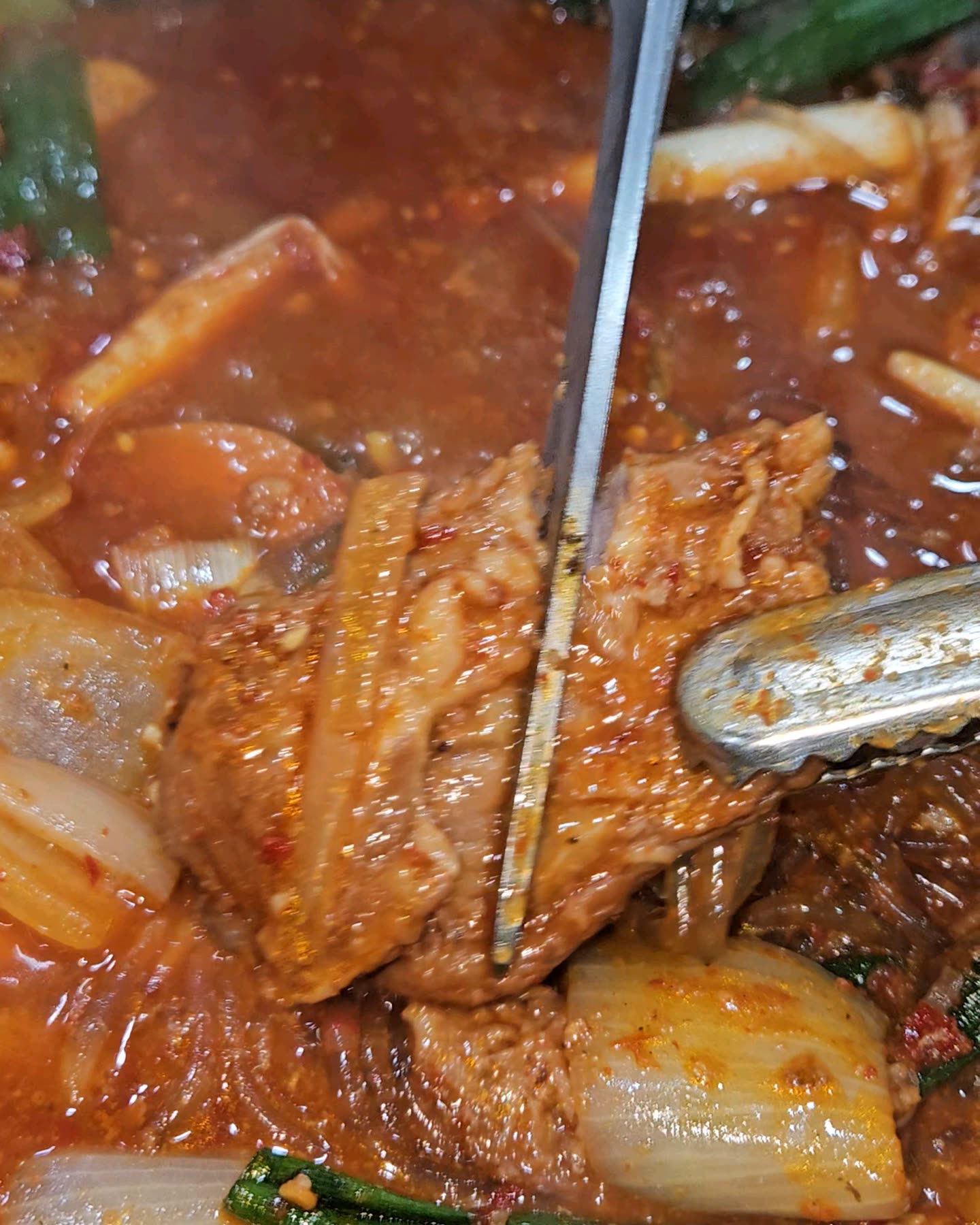 청양골송아지매운갈비찜 매운 소갈비찜에서 집게로 갈비 한 덩이를 들어 올리는 모습
