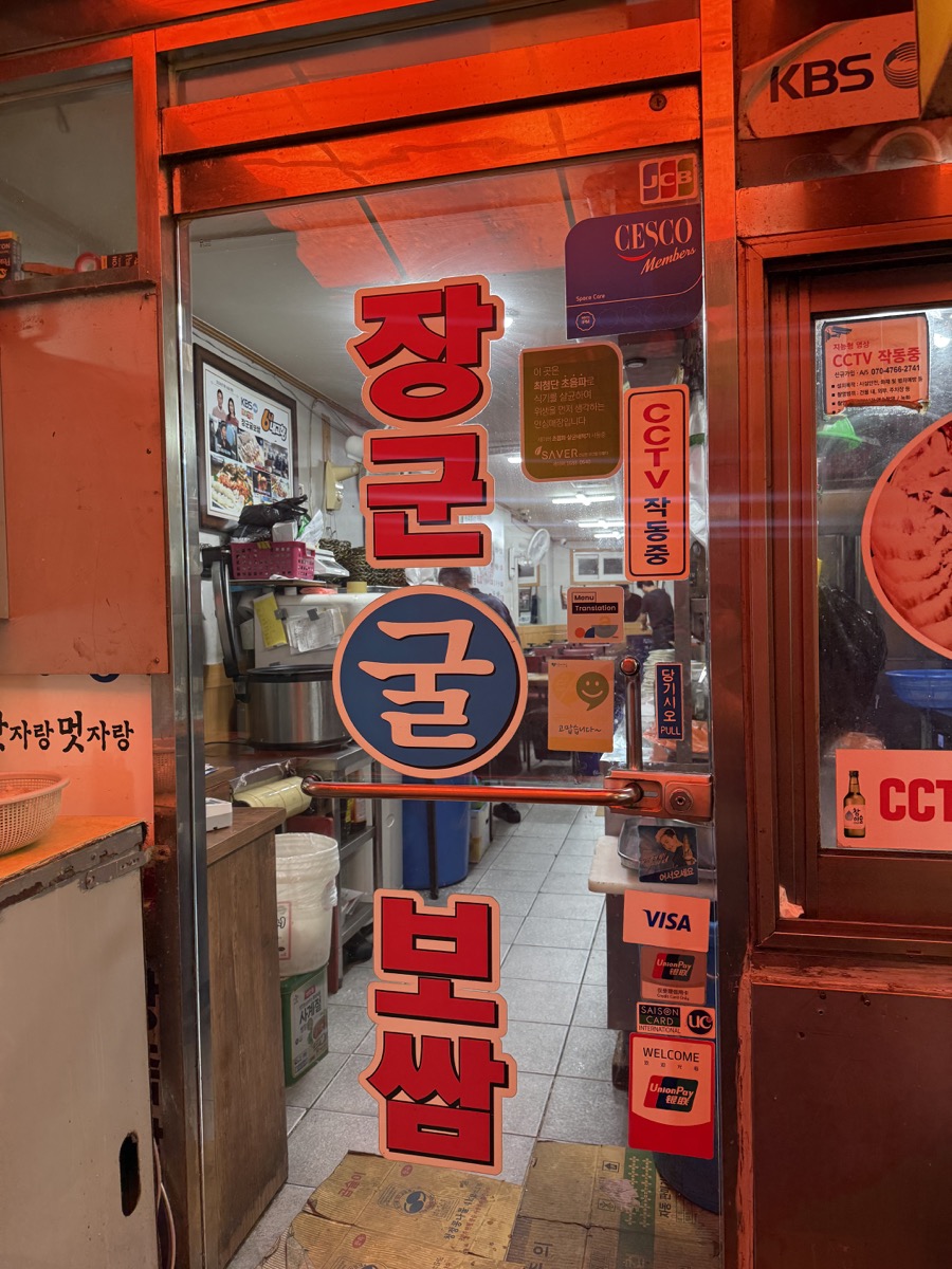 장군굴보쌈 입구, 장군 굴 보쌈 세로 간판과 KBS 방송 표시가 붙은 빨간 조명의 출입구