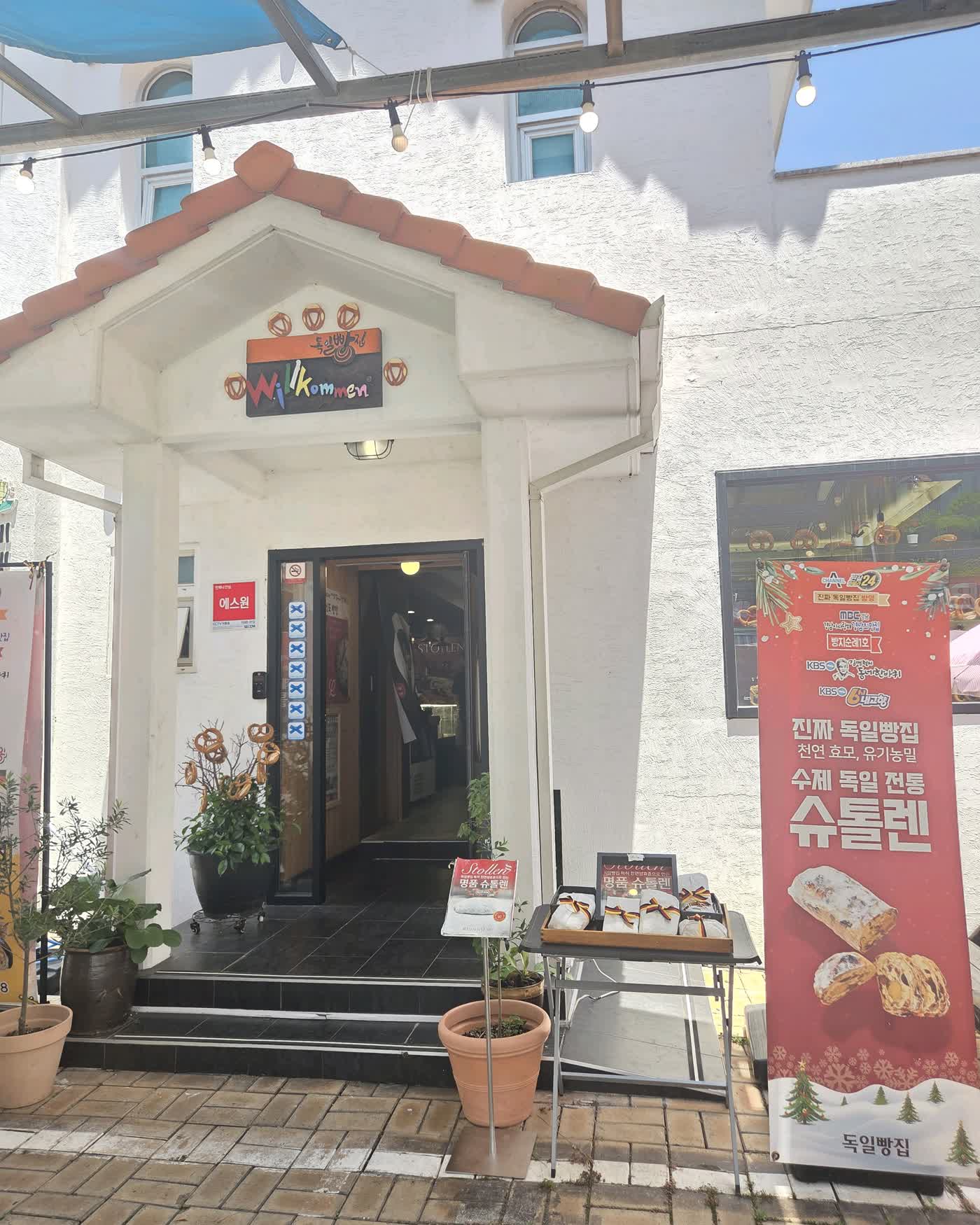 남해 독일마을 르뱅스타 독일빵집 외관, 슈톨렌 배너가 걸린 입구와 화분이 놓인 야외 테라스