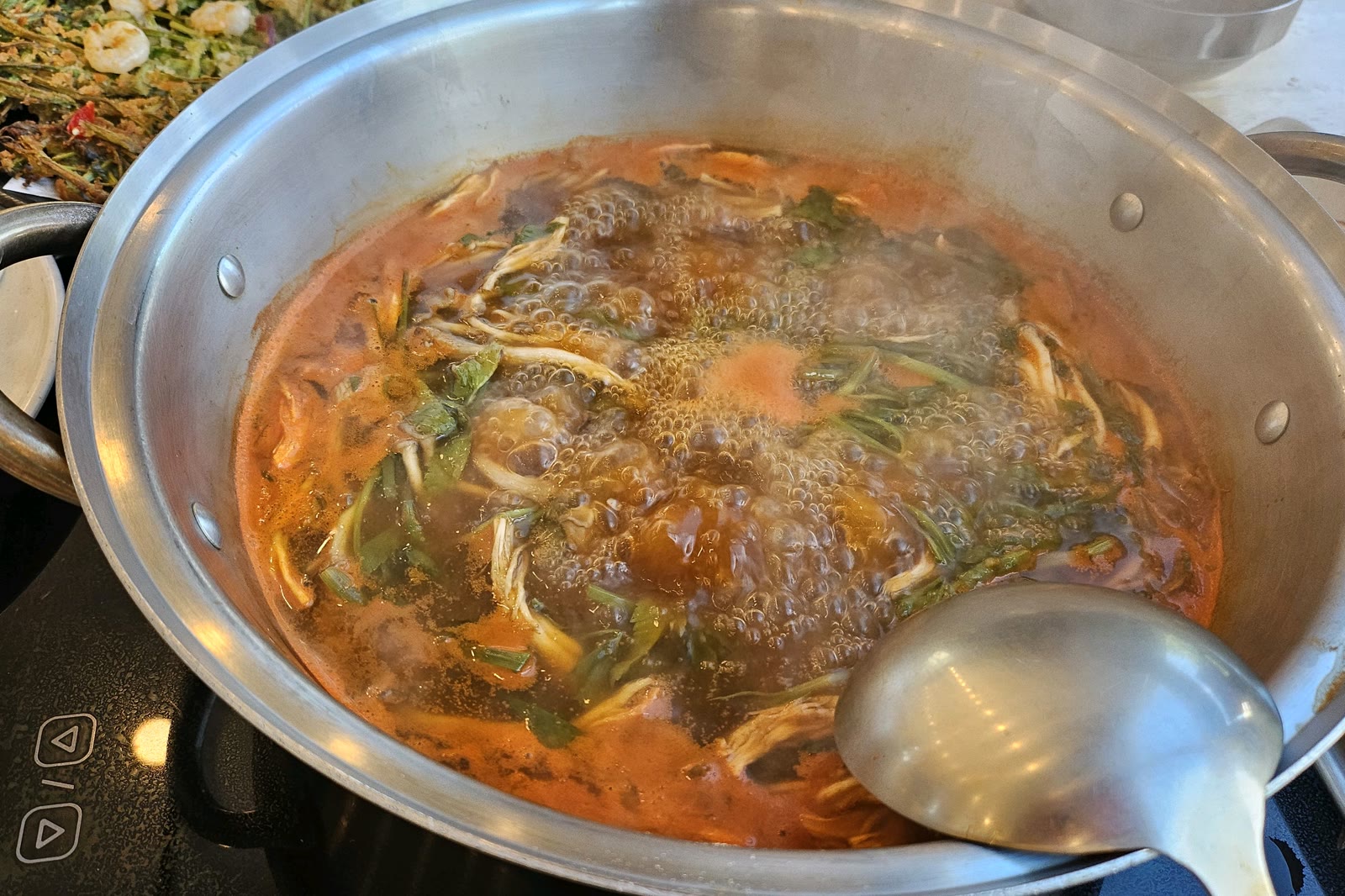 오월얼크니손칼국수 얼큰 육수가 끓는 전골에 국자를 넣은 모습, 미나리와 새우전이 함께 보이는 테이블